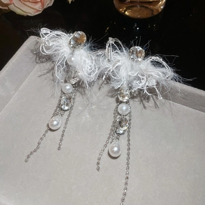 Detail shot of tassel earrings featuring white feathers and pearls on a grey display tray