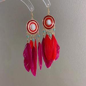 Detail of red bohemian earrings featuring layered feathers and enamel ethnic pendants