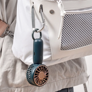 Portable dark green mini USB fan with gold grille hanging on a white backpack