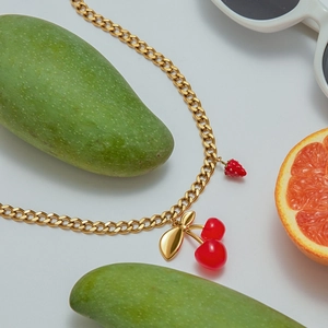 Golden necklace with red cherry and strawberry pendants styled with summer fruits