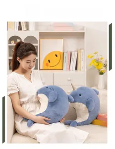 Soft plush narwhal and shark toys being held by a model on a white sofa in a cozy home setting