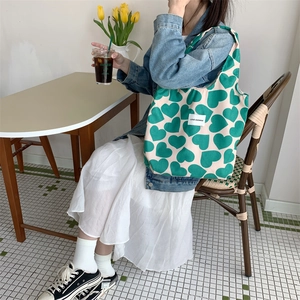 Detail of green heart pattern corduroy tote bag worn by a model in a cafe setting