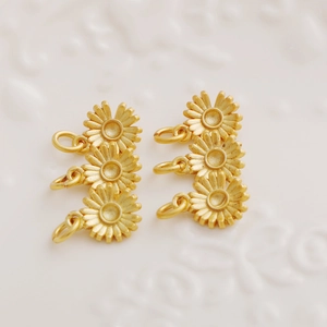 Macro shot of gold-plated sunflower charms for DIY jewelry making on white textured surface