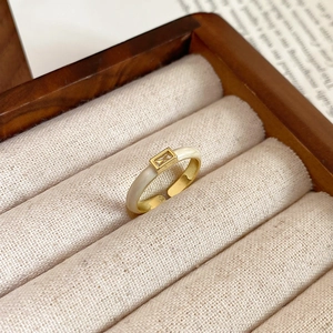 Detail of gold open ring with cream enamel and rectangular zircon on wood tray