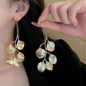 Close-up of golden metal leaf-shaped drop earrings worn by a model in warm lighting