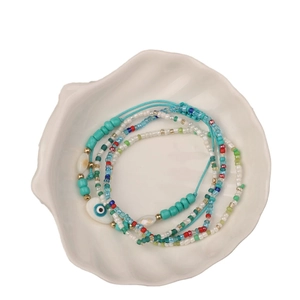 Handmade colorful seed bead bracelet with evil eye and shell charms in a white dish