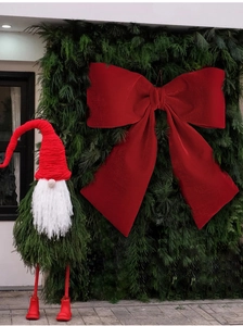 Detail of oversized red velvet bow and green foliage gnome Christmas tree decoration