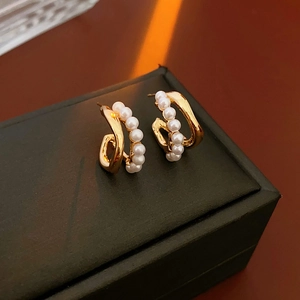 Detailed macro view of double-layered C-shaped gold earrings with white pearl accents