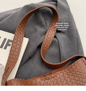 Detail of a brown woven-texture crossbody bag with smooth wide shoulder strap and fine stitching
