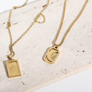 Gold-plated square sun and moon pendant necklaces on natural stone surface