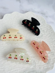 Detail view of four acetate cherry hair claws with rhinestones on a decorative ceramic tray