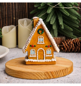 Detail of glowing LED gingerbread house on wooden tray with cozy Christmas decor