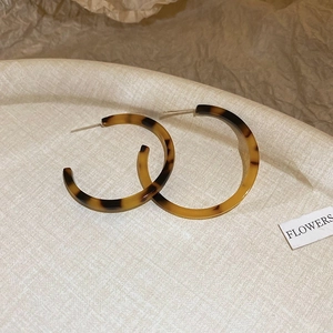 Detail shot of oversized amber leopard print resin C-shaped hoop earrings on a tray