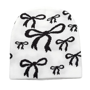 Detailed view of white knitted beanie featuring black bow patterns and ribbed texture