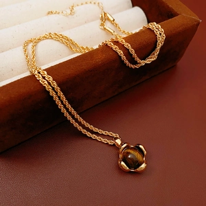 Detailaufnahme der goldenen Kordelkette mit Tigerauge-Anhänger auf Samtkissen