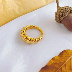 Close-up of gold titanium steel croissant ring with twisted rope texture on white fabric