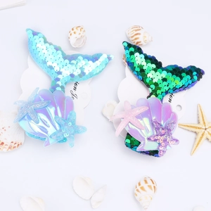 Flat lay of sequined mermaid tail hair clips with colorful shells and starfish details