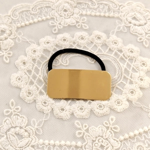 Detail of a minimalist rectangular gold metal hair tie on a white lace background