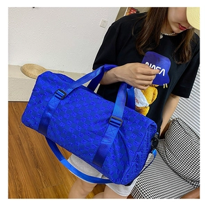 Large blue checkered travel duffel bag being carried by a model in a casual indoor setting.