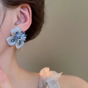 Detail view of blue crystal flower earrings worn by a model with delicate pearl accents
