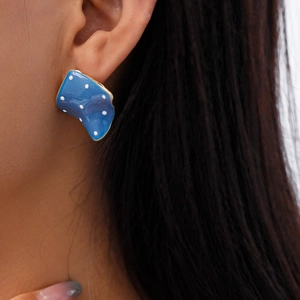 Close-up of irregular square earring with blue enamel, white dots and gold trim