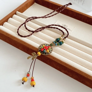 Detailed close-up of ceramic beads and bronze leaf charms on a woven ethnic necklace