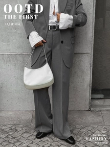 Close-up of minimalist white half-moon shoulder bag styled with casual grey business suit