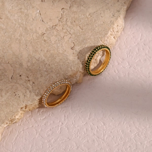 Close-up of gold rings with micro-pave green and white zircons on a beige stone base