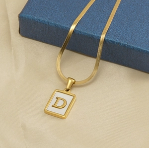 Macro detail of gold square shell necklace pendant featuring letter D on a snake chain