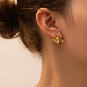 Close-up of a vintage golden bee stud earring with a pearl on a female model's ear