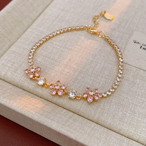Macro detail of gold flower bracelet with pink zircon petals and white crystal accents