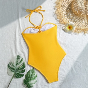 Flat lay of yellow drawstring cutout swimsuit with white hibiscus and tropical leaves