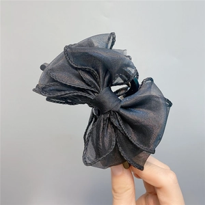 Detail of a large black organza bow hair claw clip held by hand against a grey background