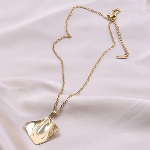 Detailed view of gold 18k plated stainless steel leaf pendant on white silk fabric
