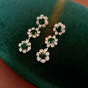 Detail of silver drop earrings with green gemstones on green velvet background