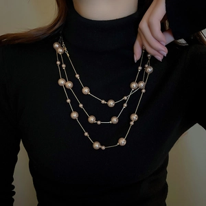 Elegant multi-layer gold chain necklace with champagne pearls over a black sweater