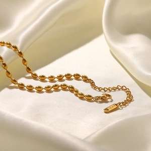 Macro shot of oval golden beads on a stainless steel chain over white silk fabric