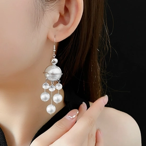 Close-up of long silver planet pearl and zircon tassel earrings on model