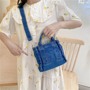 Detailed view of dark blue denim tote bag with detachable strap shown on a model