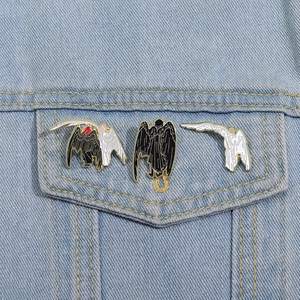 Good Omens style angel and demon enamel pins on blue denim fabric background