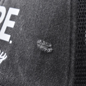 Macro detail of distressed cotton fabric and mesh structure on black NOPE trucker hat