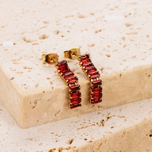 Elegant gold earrings with square red zircon stones on a beige textured stone surface