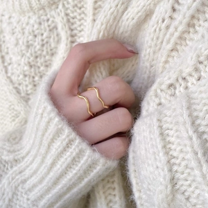 Detail of a gold wavy double-layered ring worn by a model on a white knit background