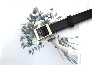 Close-up of black faux leather skinny belt featuring a square golden buckle and fine stitching
