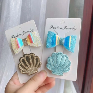 Close-up of glitter bow and shell hair clips with rainbow laser finish on paper cards