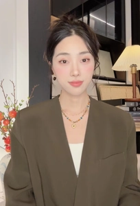 Détail d'un collier de perles multicouche avec pendentif soleil doré sur blazer vert