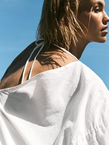 Relaxed V-neck cotton dress with tie-back detail against a clear blue sky background