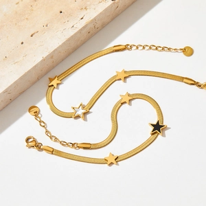 Detail of gold snake chain bracelets with black and white star charms on stone