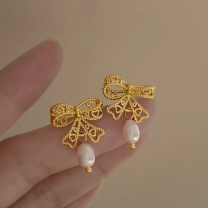 Close-up of golden hollow bow earrings with elegant white teardrop pearl pendants