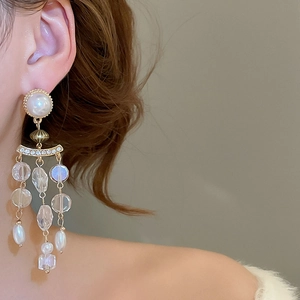 Close-up of golden pearl and crystal tassel earring worn by a model in soft lighting